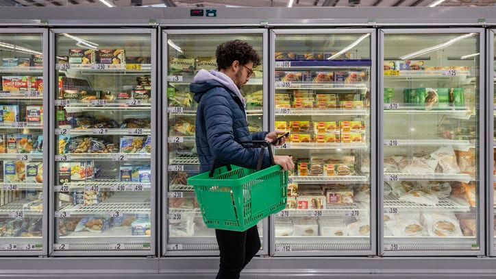 A man is standing in front of a fridge in a supermarket.