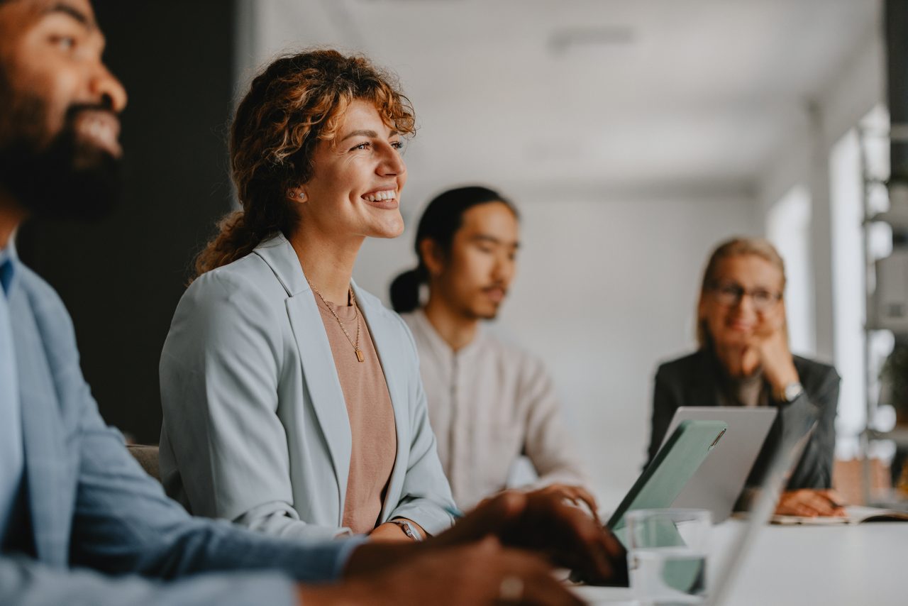 A diverse group of business professionals engaged in a collaborative meeting at a modern office. They are working together, sharing ideas, and using laptops.