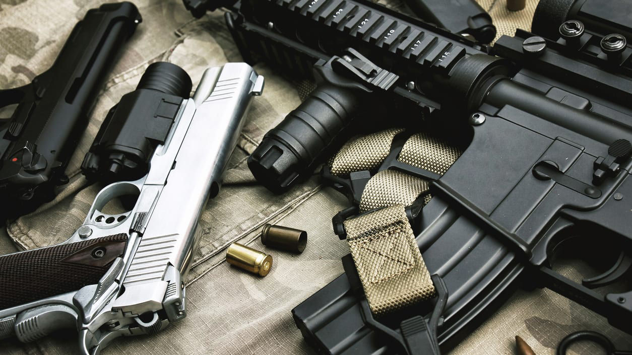 A group of firearms laying on a camouflage cloth.