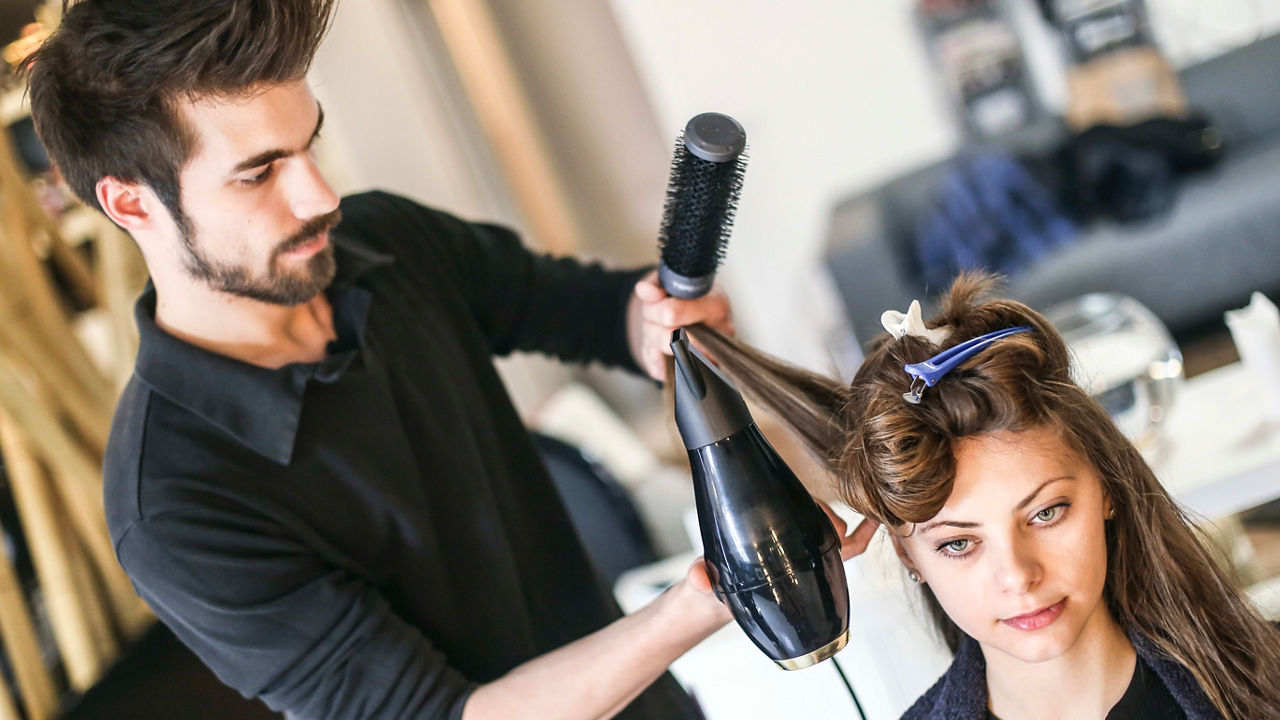 A man is drying a woman's hair in a salon.