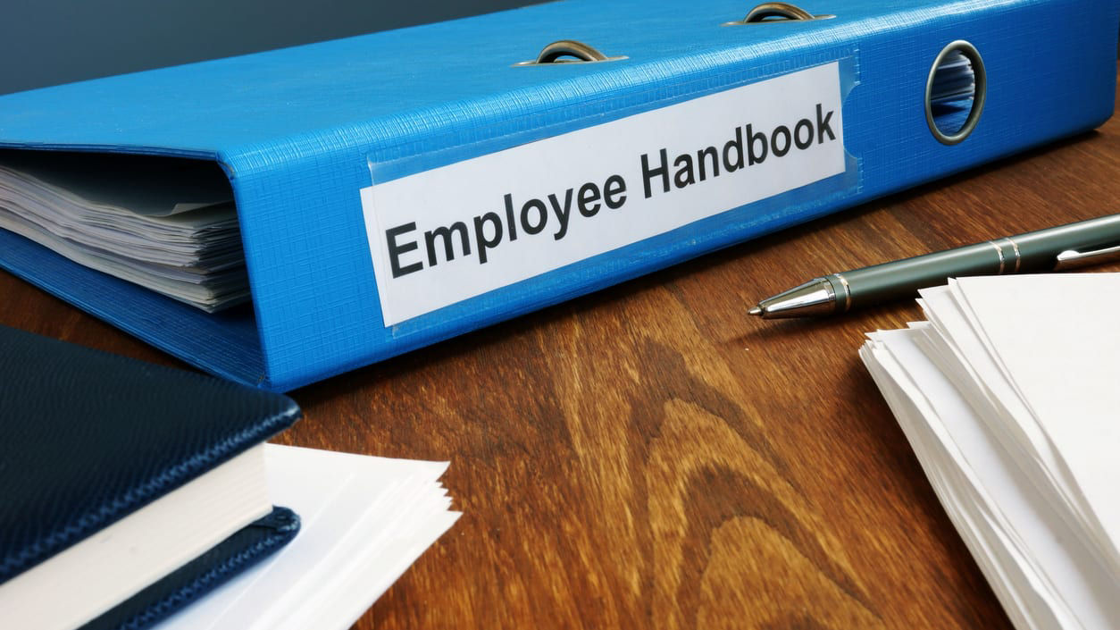 Binder on desk reading 'employee handbook'