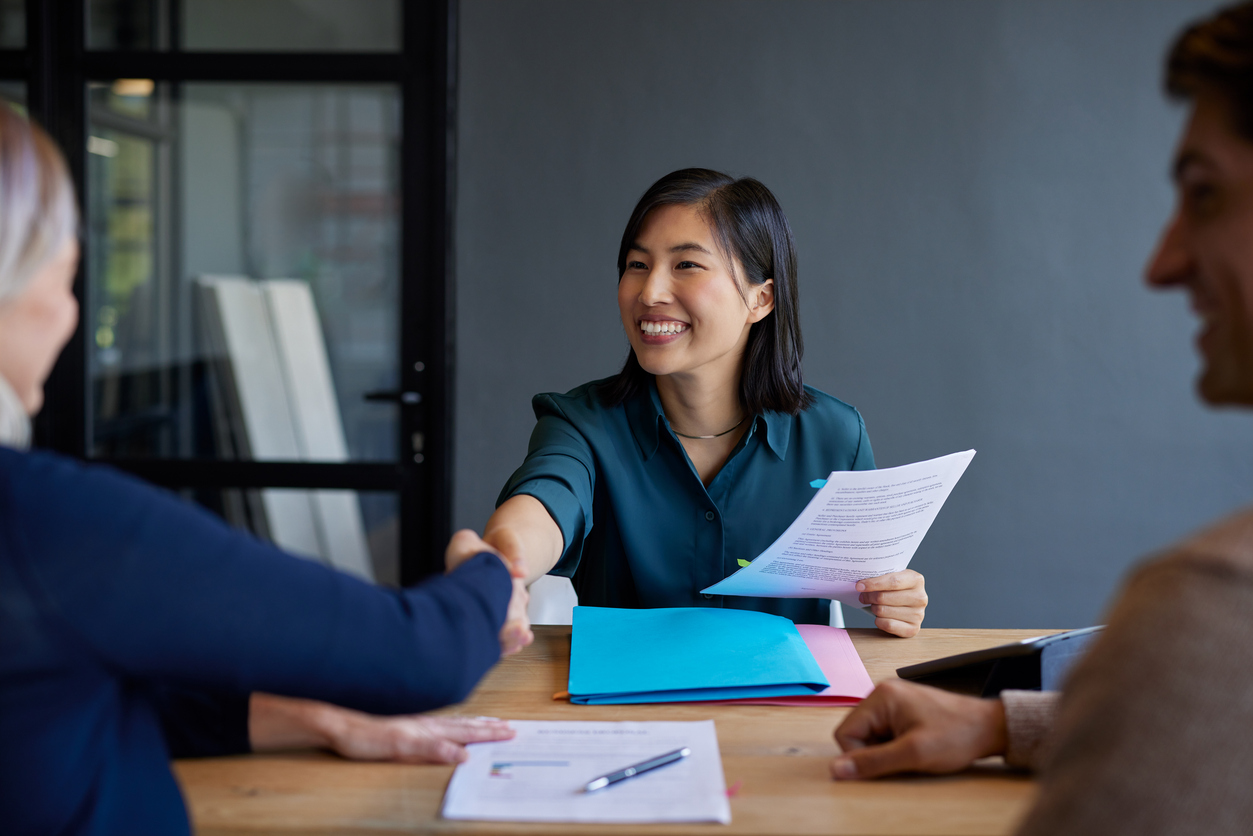 Smiling chinese candidate shakes hands during a job interview with female boss. Professional interview with candidate presenting documents. Financial advisor shaking hands after meeting a couple interested in new investments.