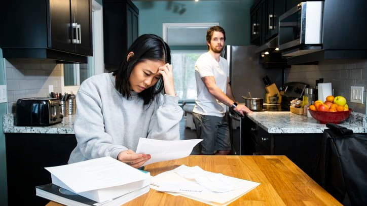 A man and woman in a kitchen with papers in front of them.