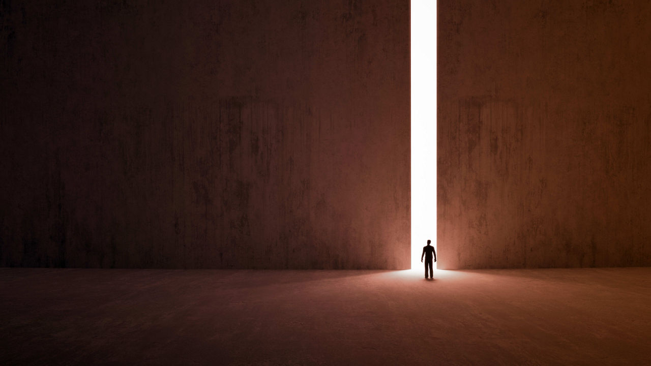 A man standing in a dark room with a light shining through a door.