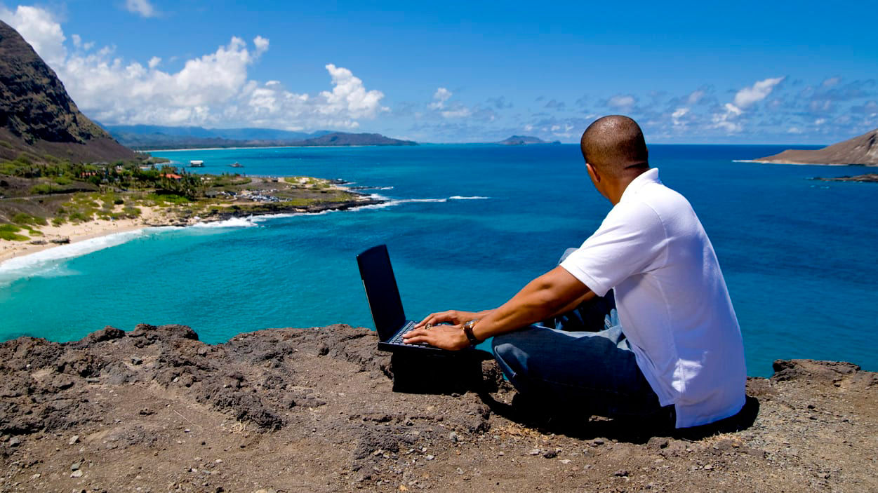 A man sitting on a cliff with a laptop.