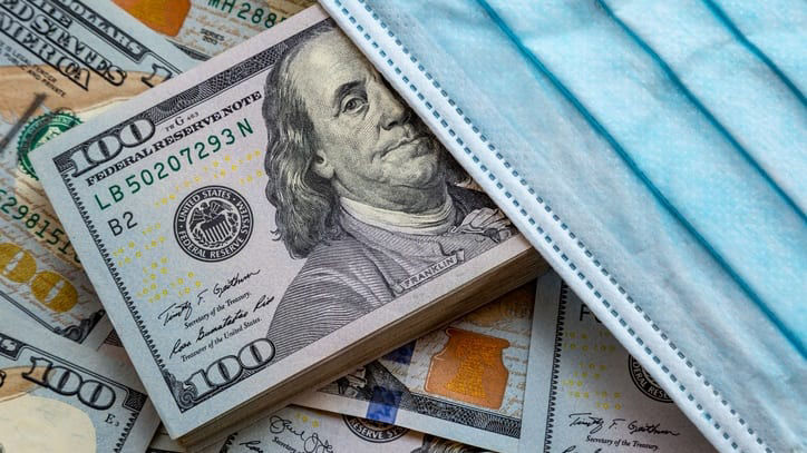 A medical mask is sitting on top of a pile of money.