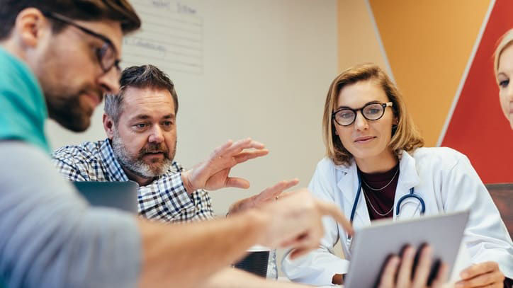 A group of people sitting around a table and looking at a tablet.