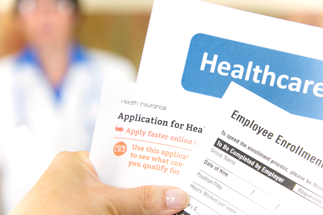 Open enrollment healthcare benefits forms with a medical doctor in the background.  Healthcare remains an important topic around the world!