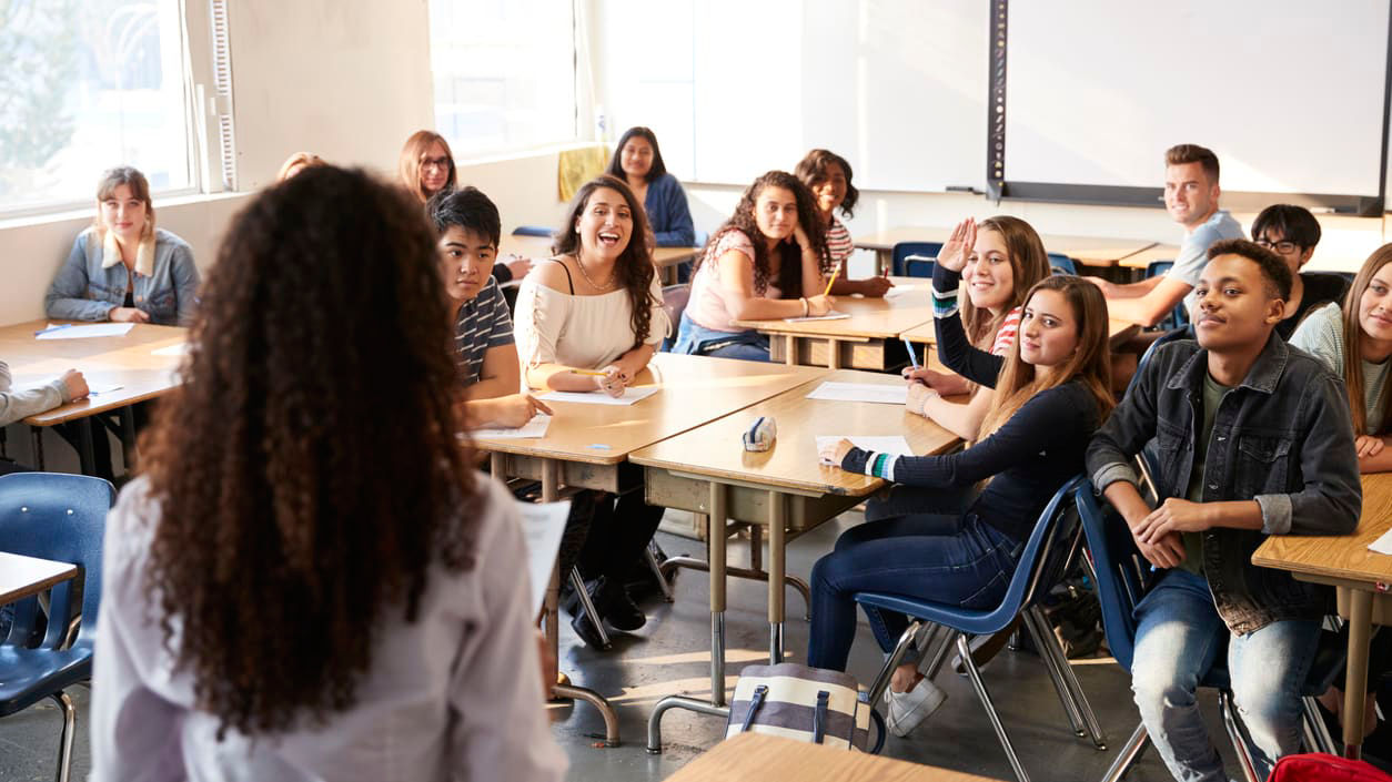 A group of students in a classroom listening to a teacher.