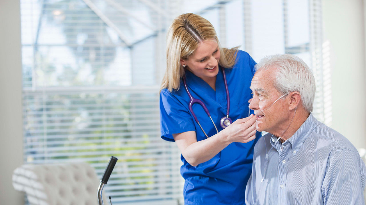 A nurse is giving an elderly man a mouthwash.