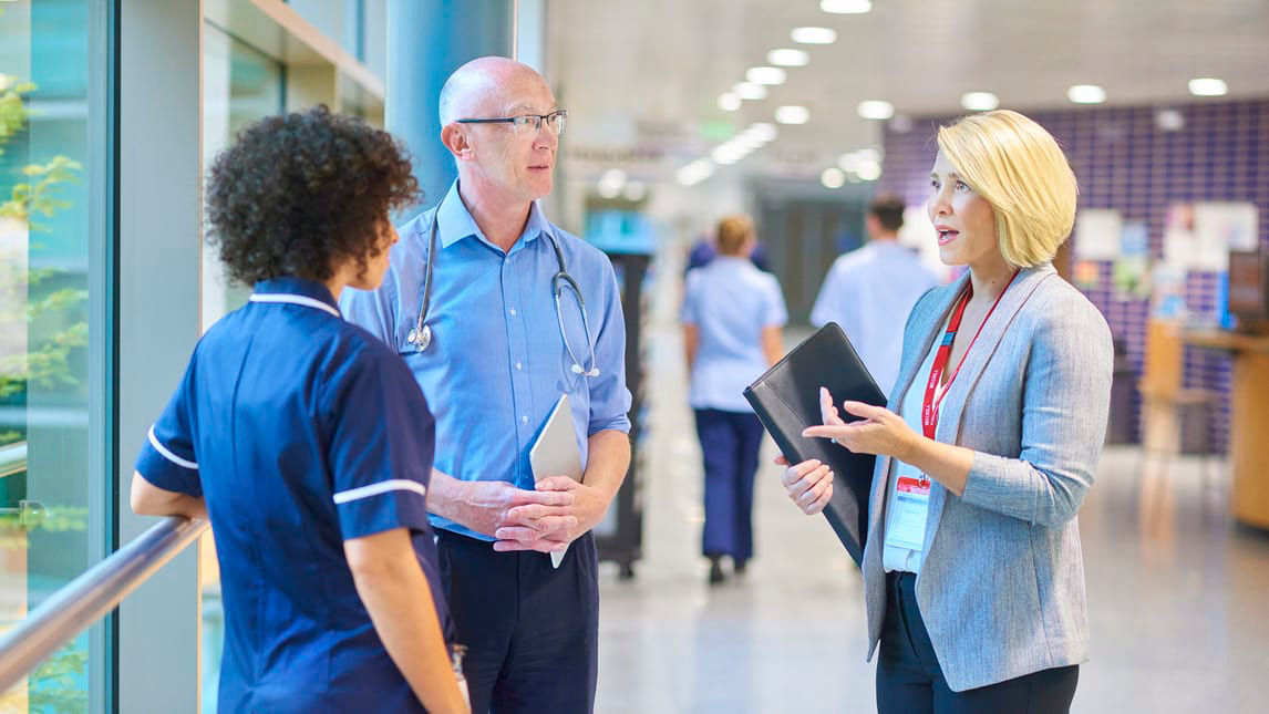 Two nurses talking to each other in a hallway.