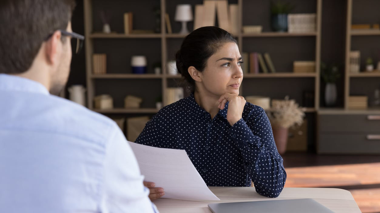 A man and woman sitting at a desk talking to each other.
