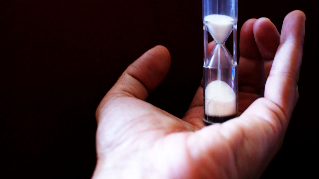 A person's hand holding a sand hourglass.