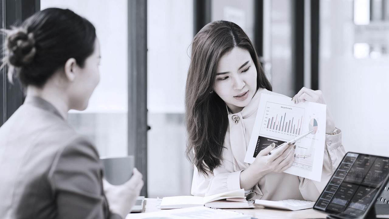 Executive pointing to HR metrics printout in conversation while sitting across the table from a business leader