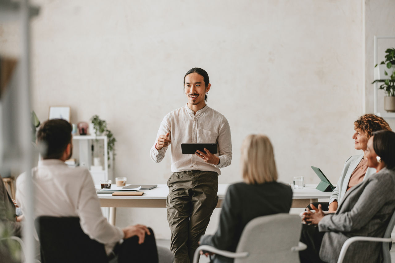 Man in informal office environment speaking to colleagues whose backs are to the camera