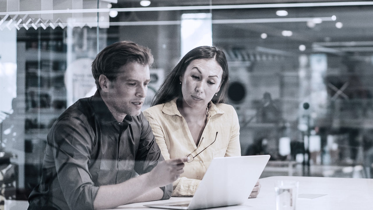 Two coworkers sitting together looking at laptop in office