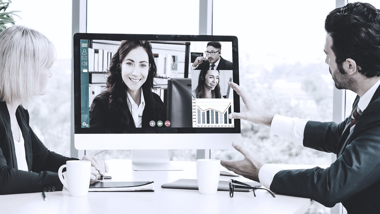A group of people sitting at a desk with a computer screen showing a video conference.