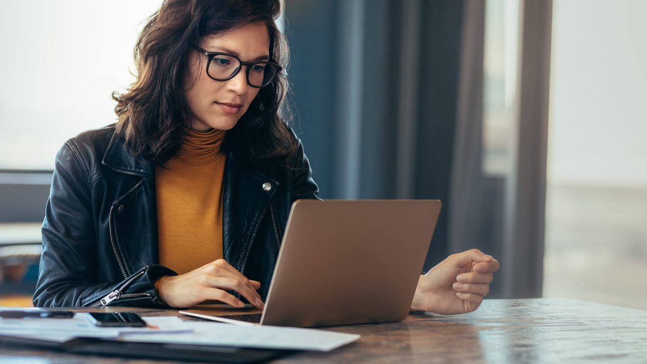 A woman in glasses is using a laptop at a table.