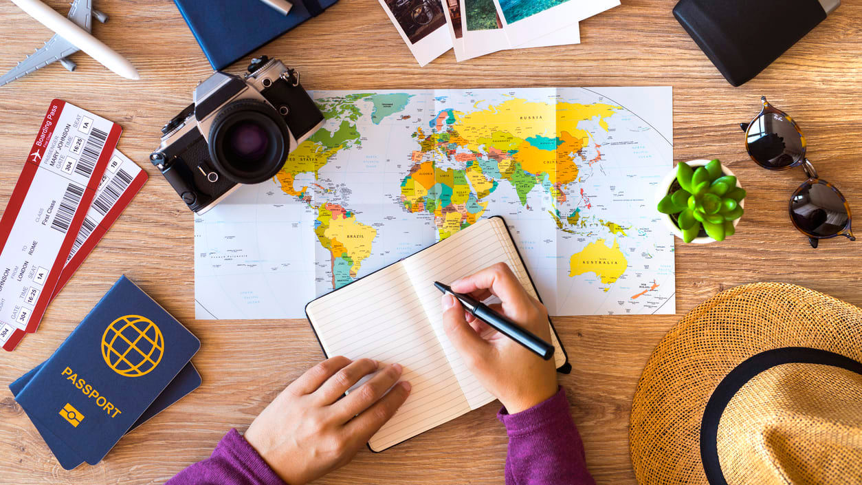 A woman is sitting at a table with a map, hat, and other travel items.