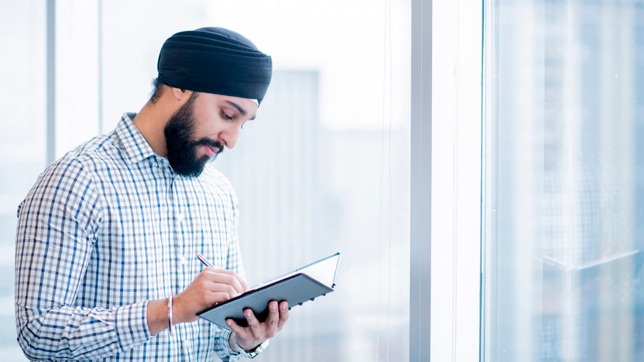 A man in a turban is writing on a tablet.