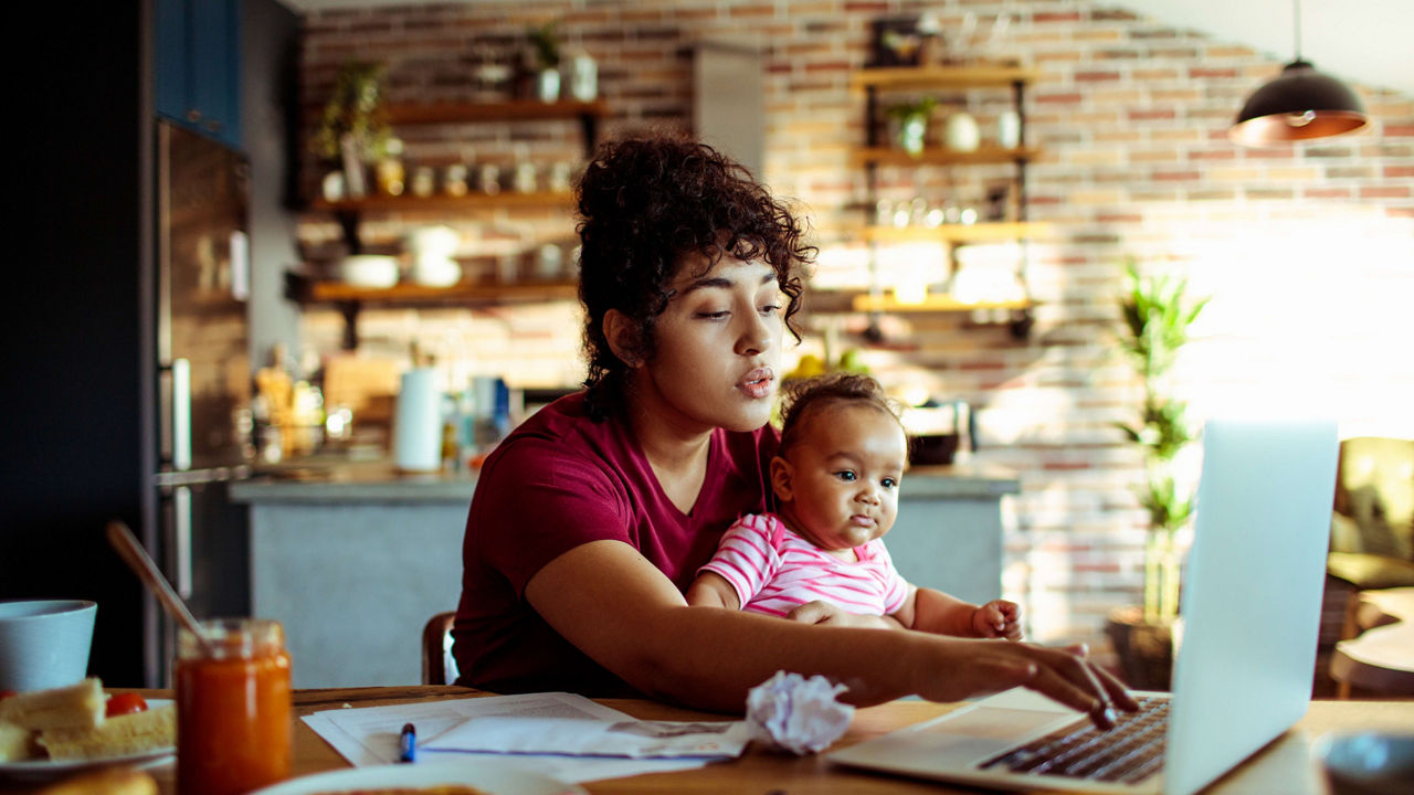 A woman working on her laptop with a baby in front of her.