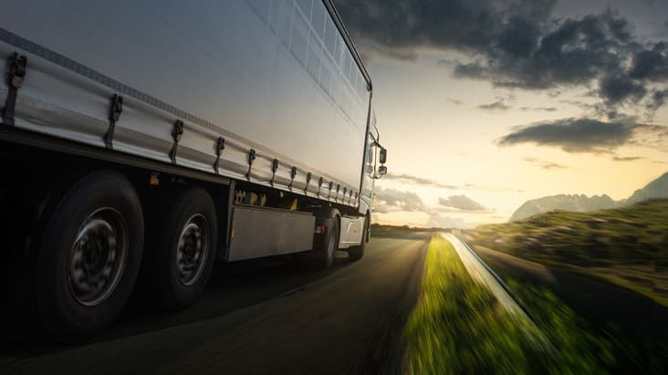 A semi truck driving down a road at sunset.