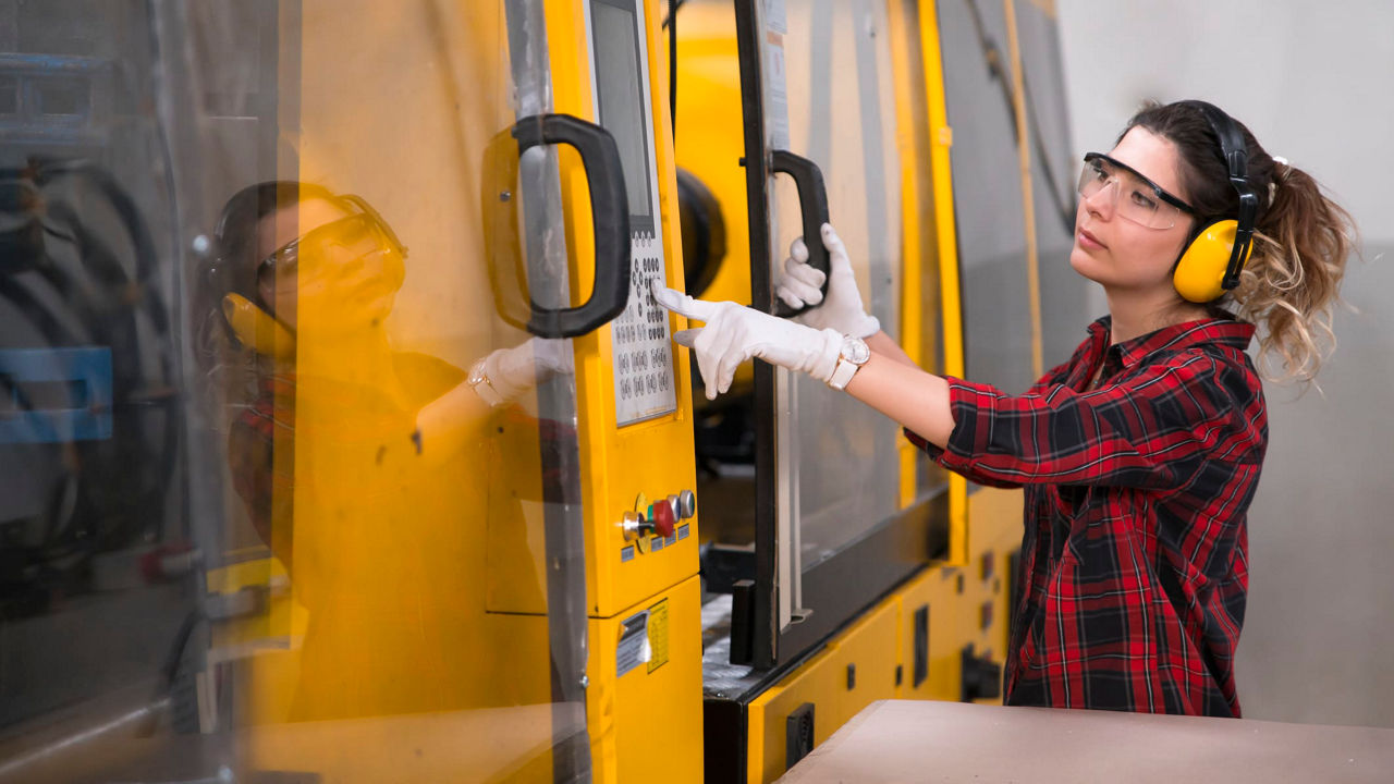 A woman wearing safety goggles is working on a machine.