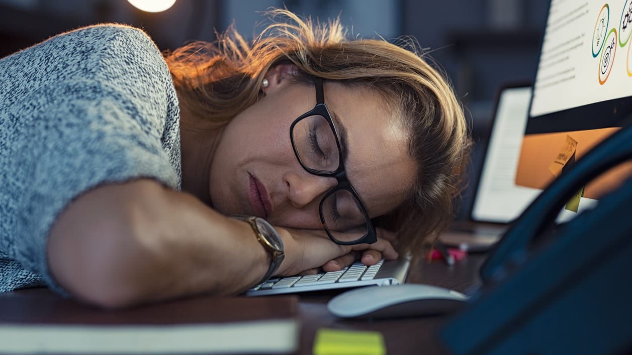 A woman is sleeping on a desk in front of a computer.