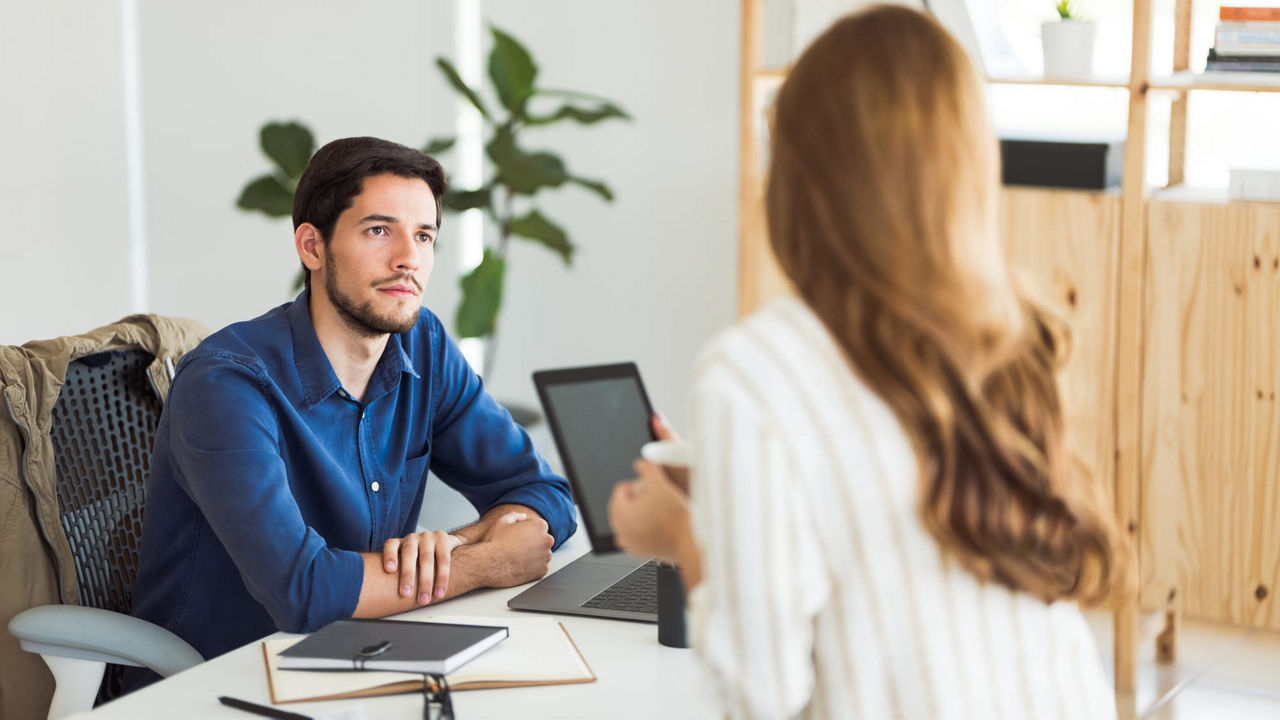 A man and woman talking at a desk in an office.