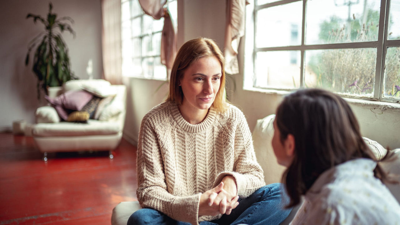 Two women sitting on a couch talking to each other.