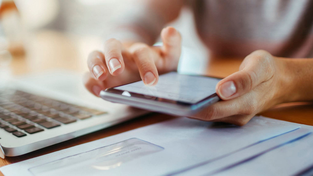 A woman's hand holding a cell phone next to a laptop.