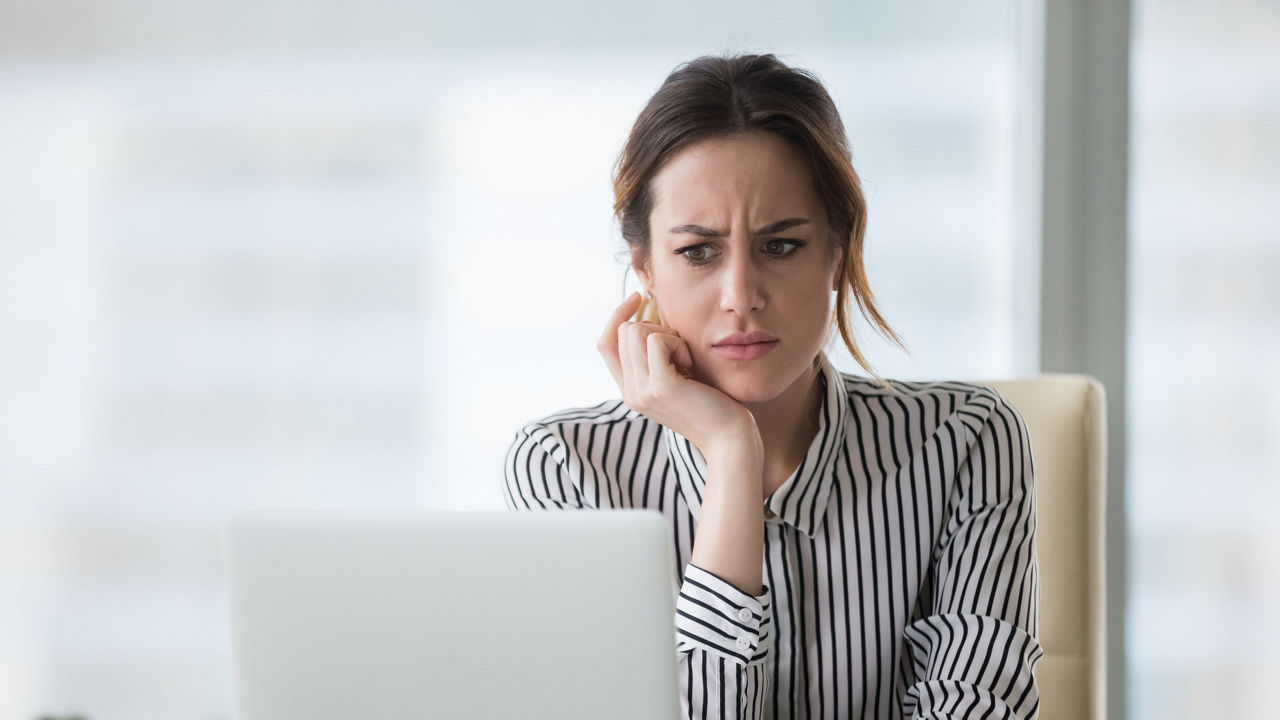 A woman sitting in front of a laptop with her hand on her chin.