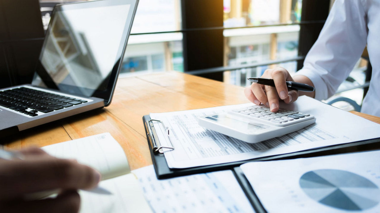 A man and woman working on a spreadsheet at a desk.