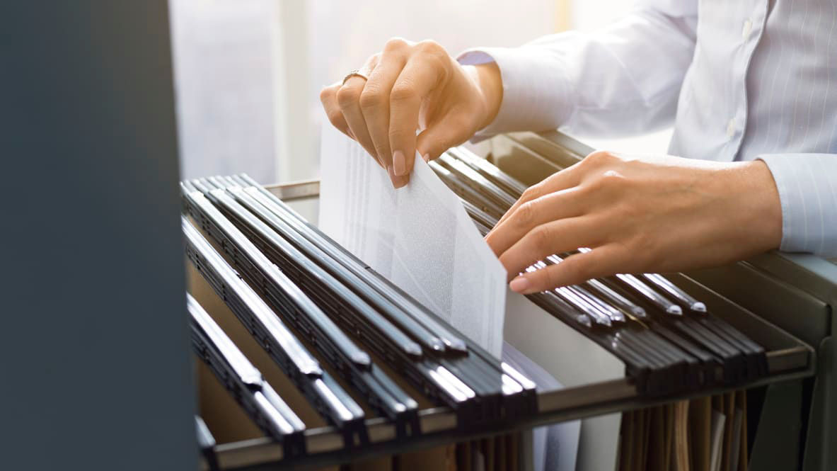 A person is putting papers into a file cabinet.