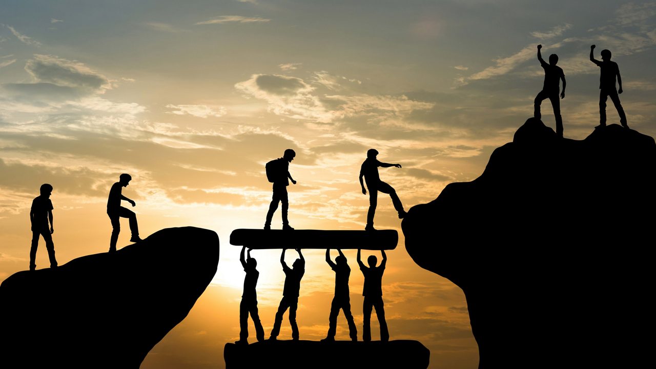 Silhouettes of people standing on top of rocks at sunset.