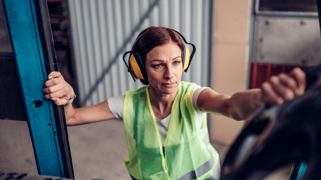 A woman wearing ear muffs is driving a truck.