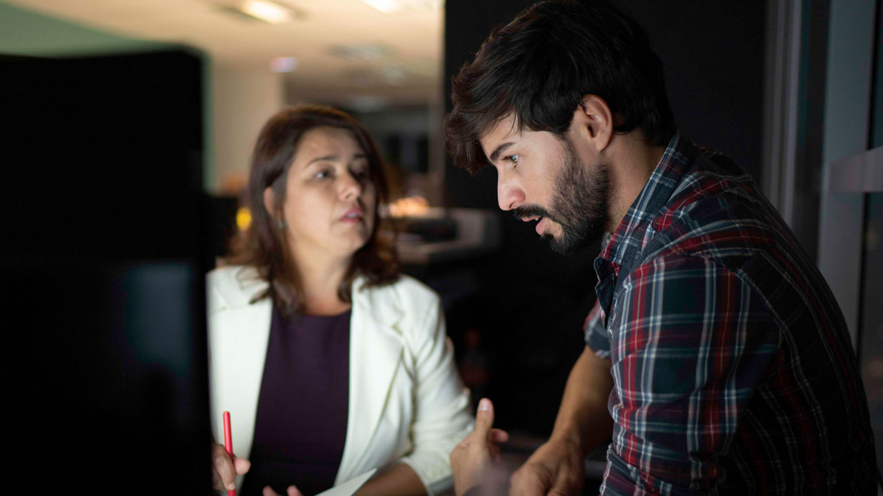 A man and woman looking at a computer screen at night.