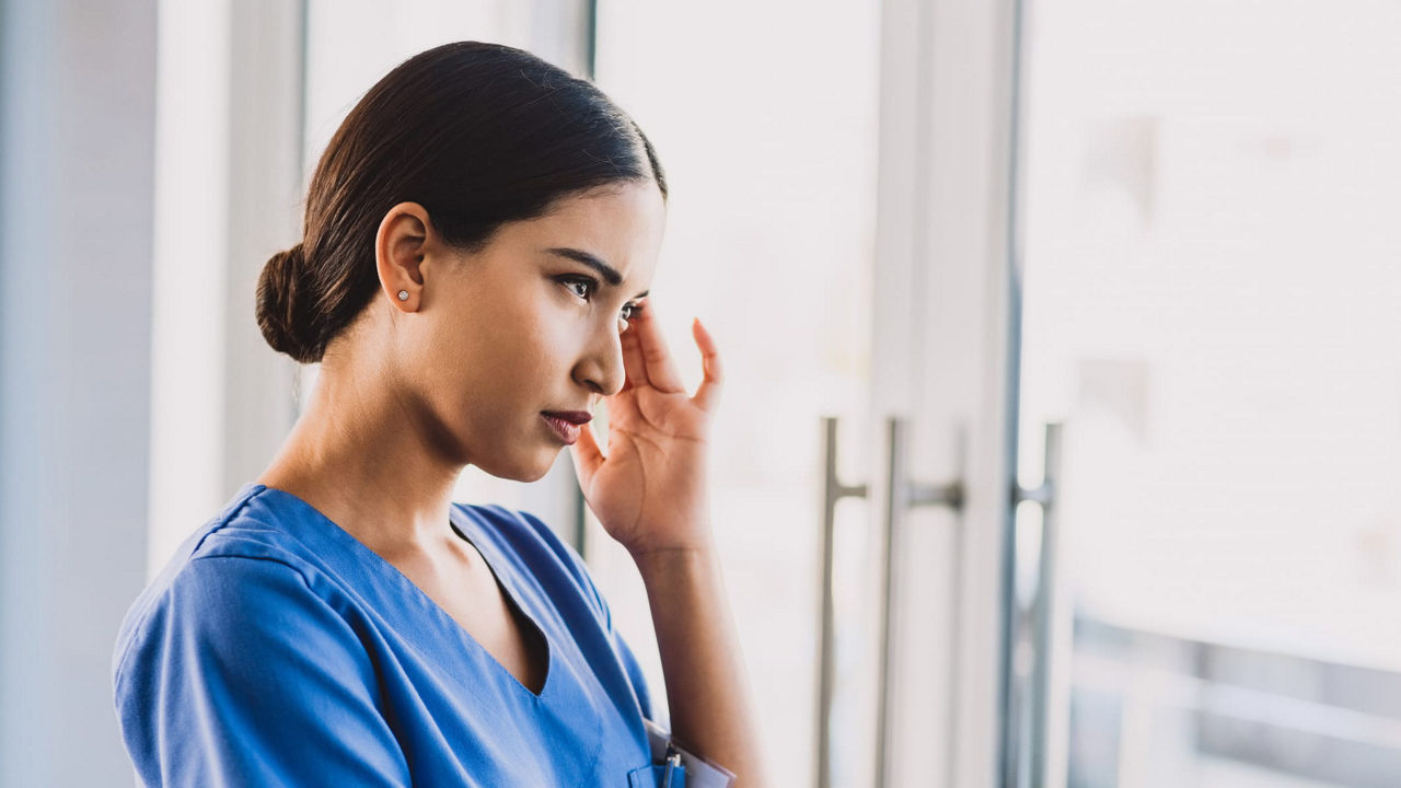 A nurse wearing blue scrubs looking out of a window.