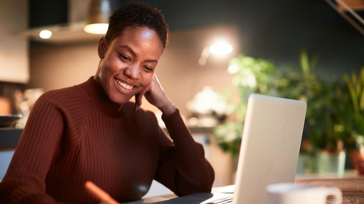 A woman writing on a laptop in front of a cup of coffee.