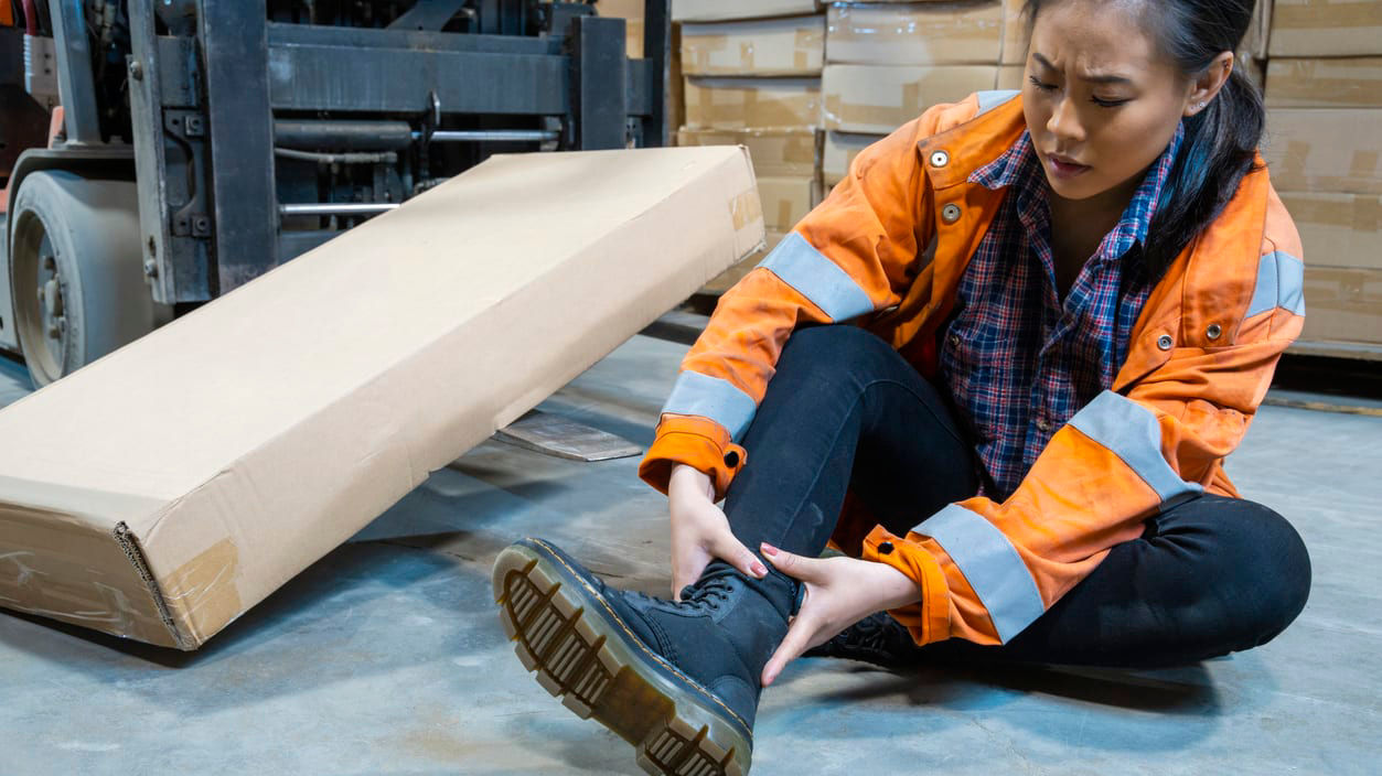 A forklift operator putting on a pair of shoes in a warehouse.
