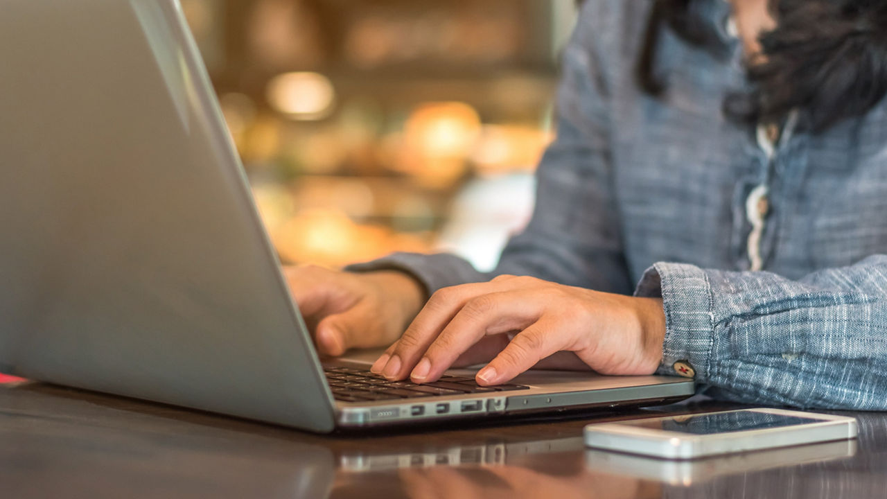 A woman is typing on a laptop at a cafe.