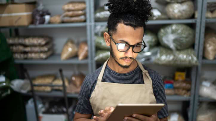 A man in an apron is using a tablet in a warehouse.
