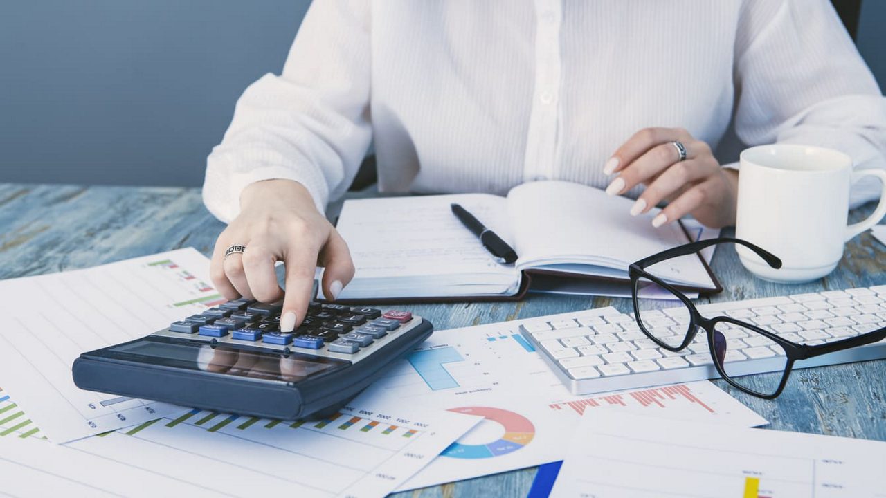 A business woman is using a calculator on a desk.