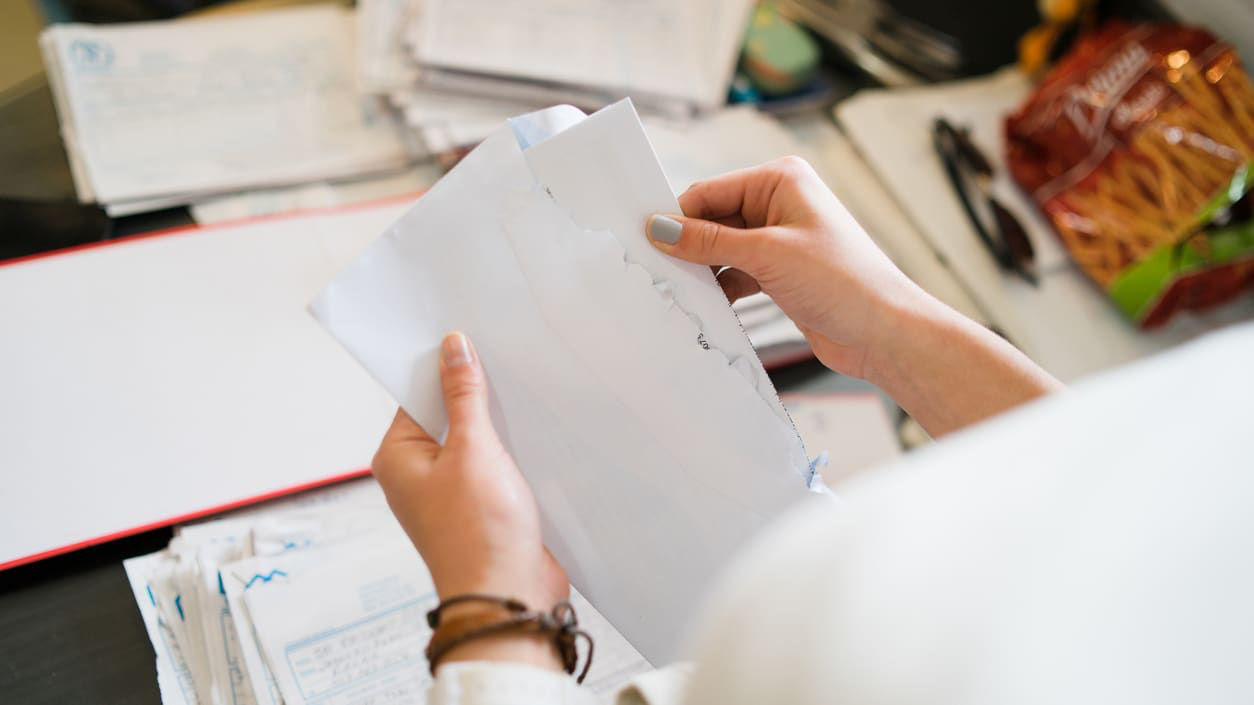 A woman is holding a piece of paper in front of a pile of papers.