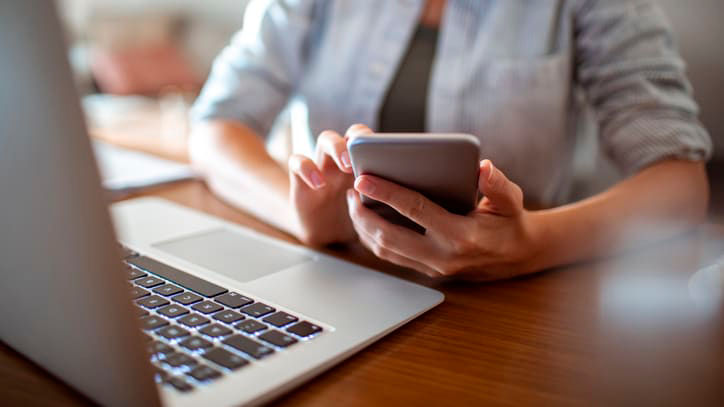 A woman using a cell phone while sitting at a desk.
