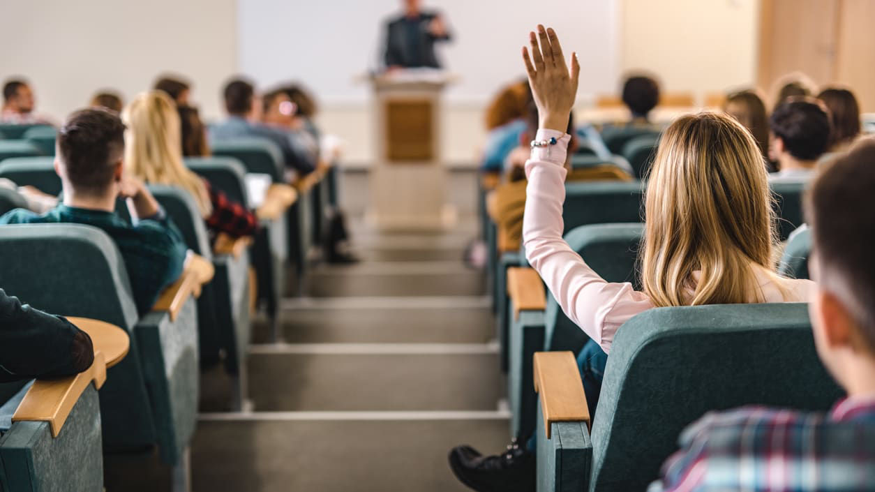 A group of people sitting in a lecture hall and raising their hands.