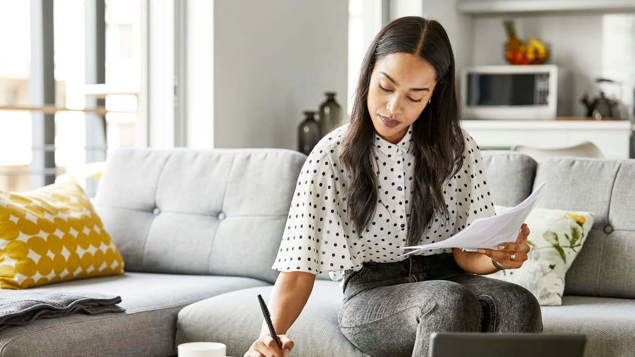 A woman sitting on a couch with a laptop and papers.