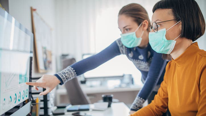 Two women wearing face masks working on a computer.
