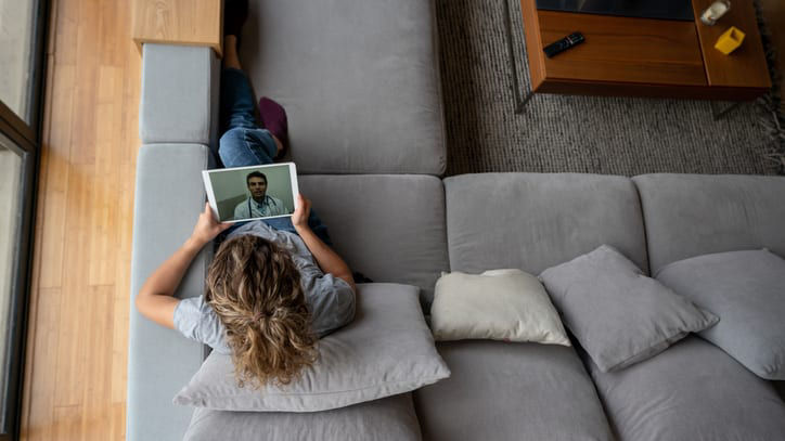 A woman is sitting on a couch and using a tablet.