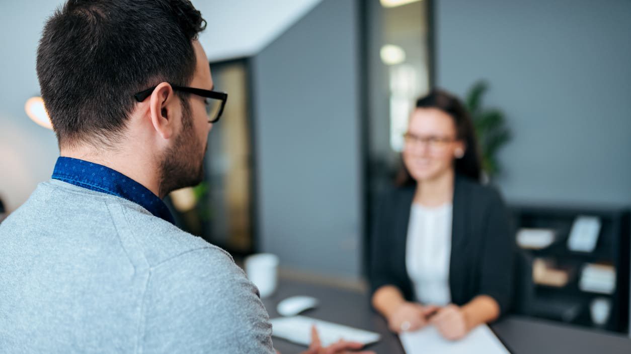 A man and woman talking at a desk in an office.